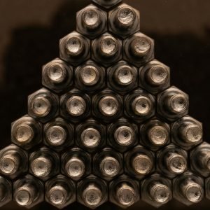 Close-up view of metallic nuts arranged in a triangular shape with a reflective surface.