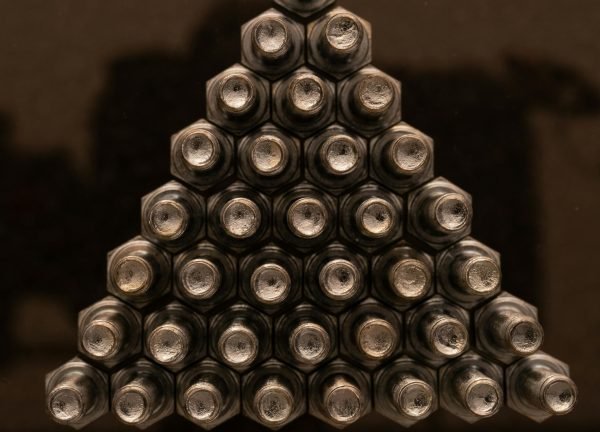 Close-up view of metallic nuts arranged in a triangular shape with a reflective surface.